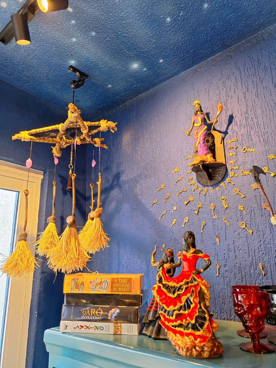 Canto da loja com parede azul, estrelas no teto, móbile de vassourinhas e imagens de Pombagira