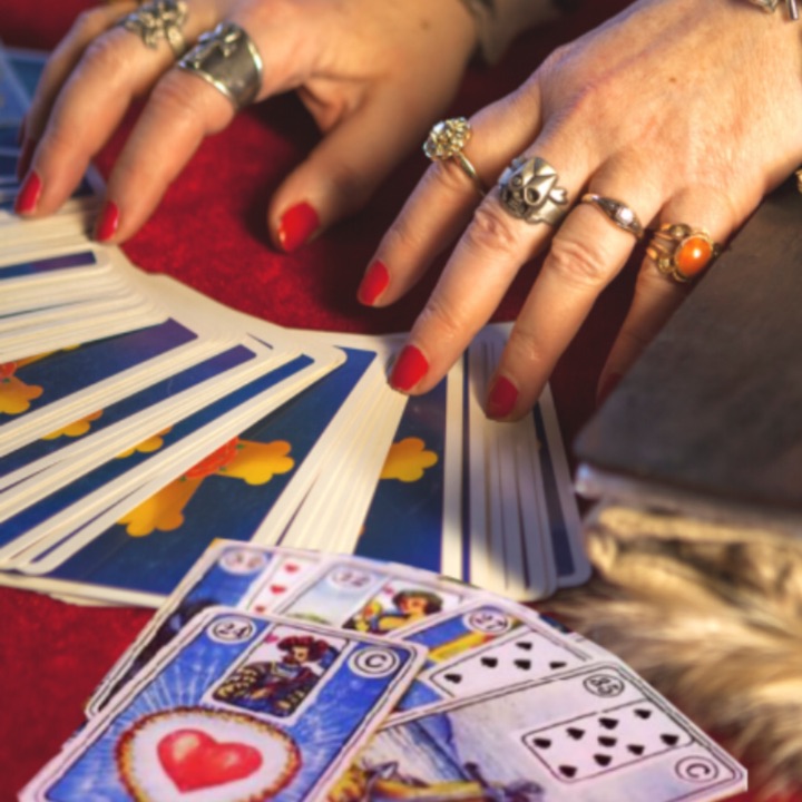 Mãos com anéis espalhando as cartas do baralho cigano sobre um pano vermelho