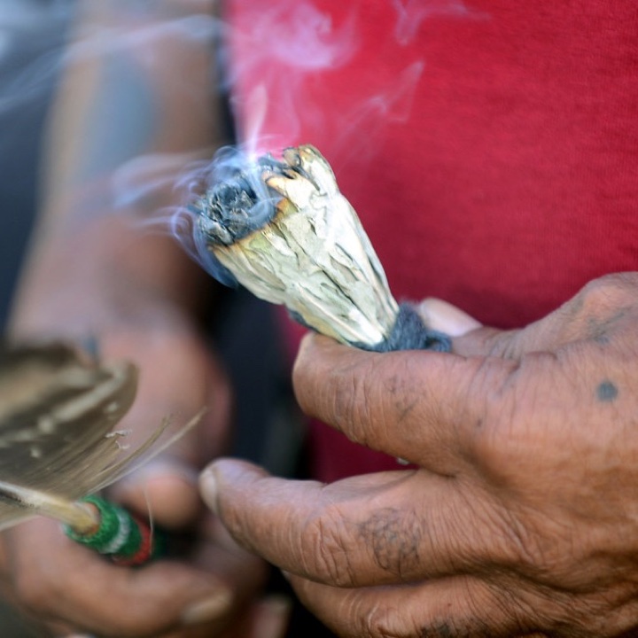 Mão segurando um maço de sálvia queimando, com a fumaça subindo