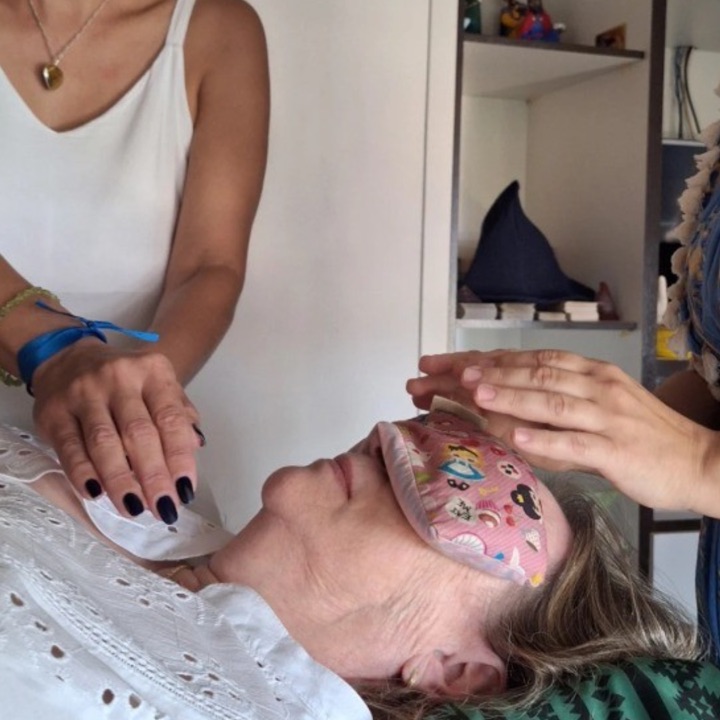 Sessão de Reiki: duas terapeutas com as mãos sobre uma pessoa deitada de olhos vendados